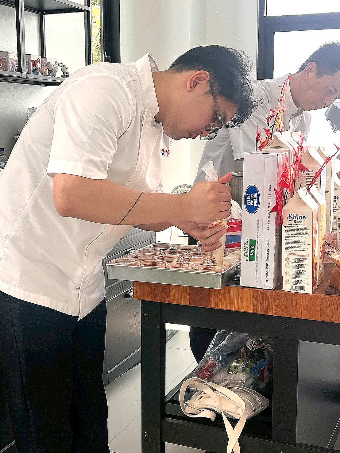 ผู้สาธิตสองคนกำลังบีบส่วนผสมลงในถ้วยขนาดเล็กที่โต๊ะด้านหน้าห้อง